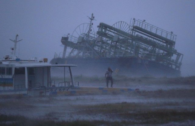 A person reacts to the weather as ship washed ashore caused by Typhoon Trami is seen at a port in Yonabaru, on the southern island of Okinawa, Japan, in this photo taken by Kyodo September 29, 2018.