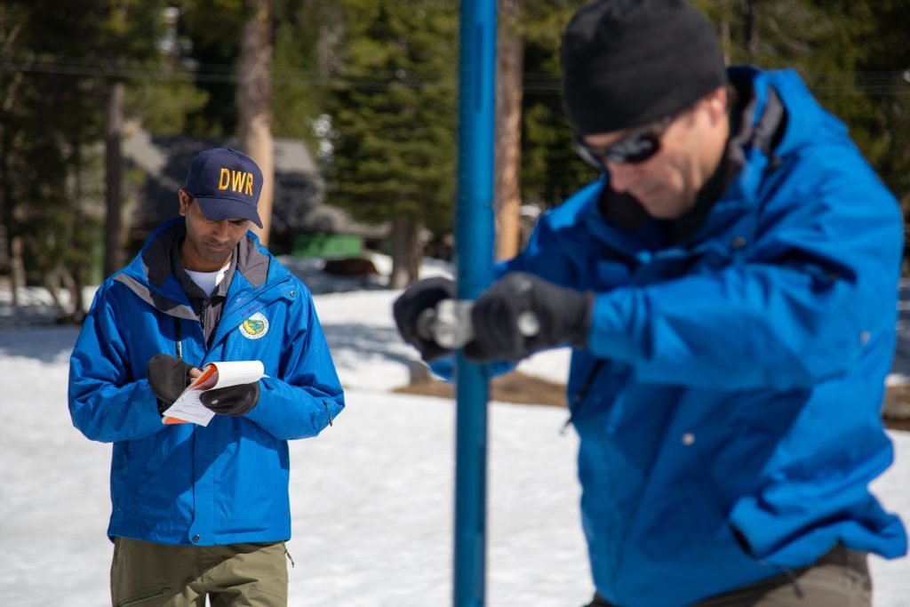 Ashok Bathulla, water resource engineer for the California Department of Water Resources, writes snow measurements as John King, Water Resource Engineer, for DWR plunges the long aluminum snow depth survey pole into the snowpack.