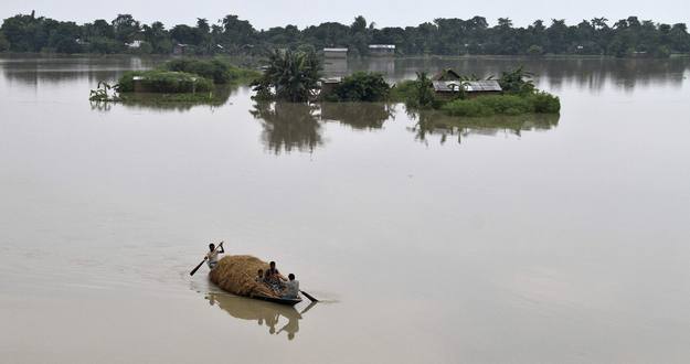 Un grupo de personas transporta paja para el ganado en un barco a través de las áreas inundadas en el estado indio nororiental de Assam