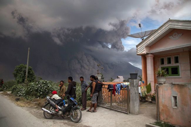 Villagers gather in front of a house as they watch Mount Sinabung releasing a pyroclastic flow during its eruption in Karo, North Sumatra, Indonesia, Wednesday, Aug. 2, 2017.