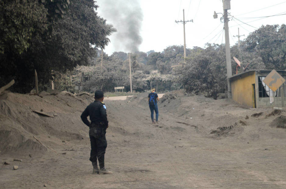 Un policía y un voluntario observan una columna de humo en la aldea de El Rodeo, cubierta de ceniza y restos de lava.