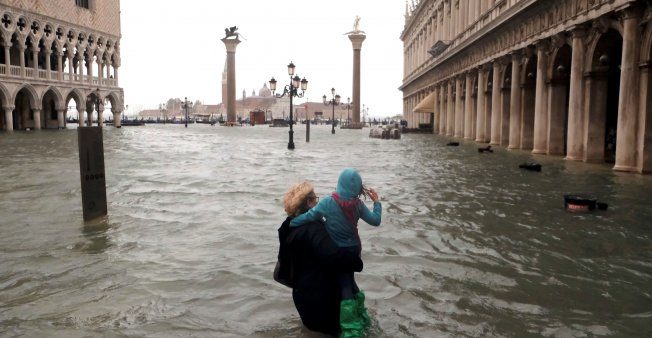Una mujer sostiene a una niña mientras camina en una plaza inundada de San Marcos durante un período de marea estacional en Venecia, Italia, 29 de octubre de 2018