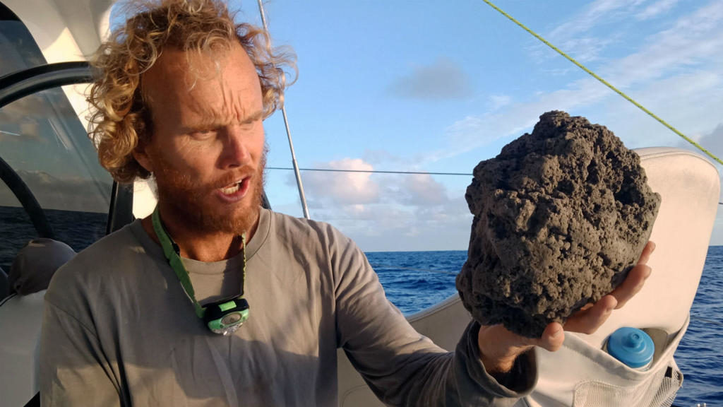 Clic para aumentar Sail Surf ROAM muestra a Michael Hoult sosteniendo grandes piezas de piedra pómez después de recogerlo de una gran balsa de piedra pómez cerca de Tonga. 26 agosto 2019.
