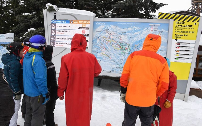 Skiers in Les Menuires check a signboard warning of avalanche risks and closed pistes C