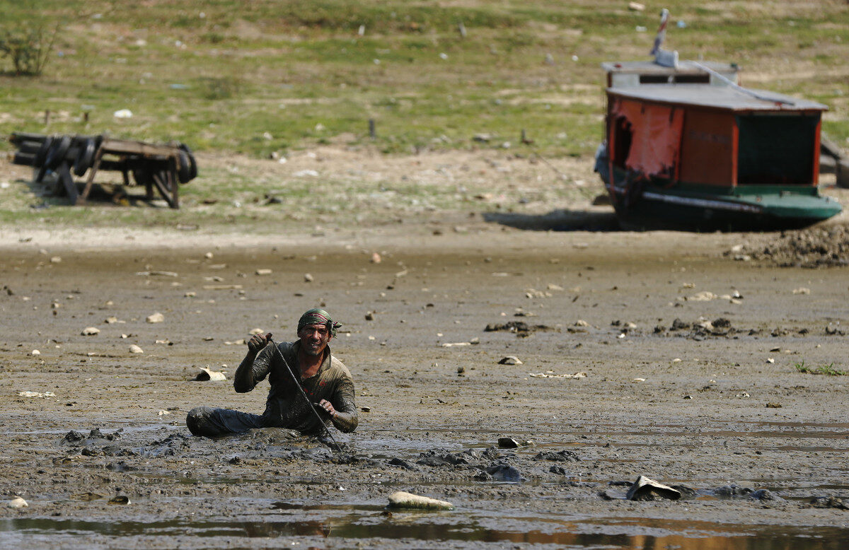 A fisherman searches for eels in the mud of the dried up Paraguay River