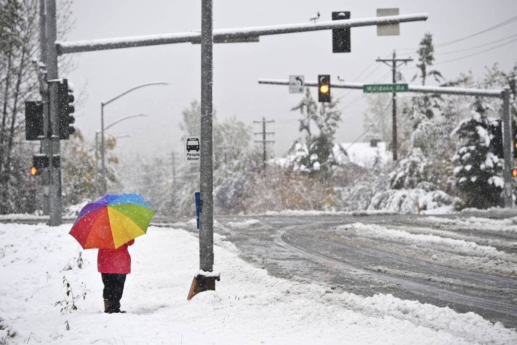 A woman waits at a bus stop on East 36th Avenue as snow falls on September 24, 2021.