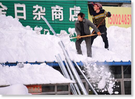 Men clear snow from a roof following heavy snowfall in Shenyang, Liaoning province, China November 9, 2021. Picture taken November 9, 2021.