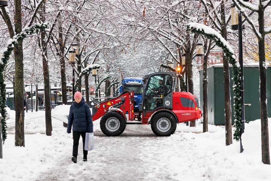 woman walks on a snowy road as a snowplow clears the road in Stockholm, Sweden on Nov. 21, 2022.