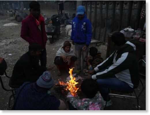 People sit around a bonfire to warm themselves during a cold winter morning, in New Delhi