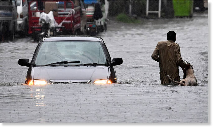 A man along with his dog while a car wade through a flooded street during heavy monsoon rains in Rawalpindi on July 17, 2025.