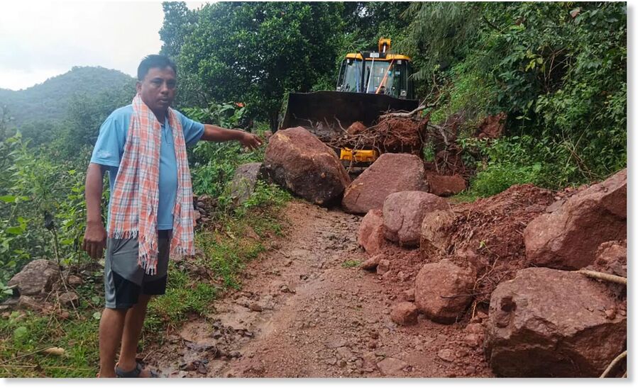 A man points at boulders that fell during a landslide as a bulldozer clears debris from a road, at Linga village, in Gajapati district, Odisha, Wednesday, Oct. 29, 2025.