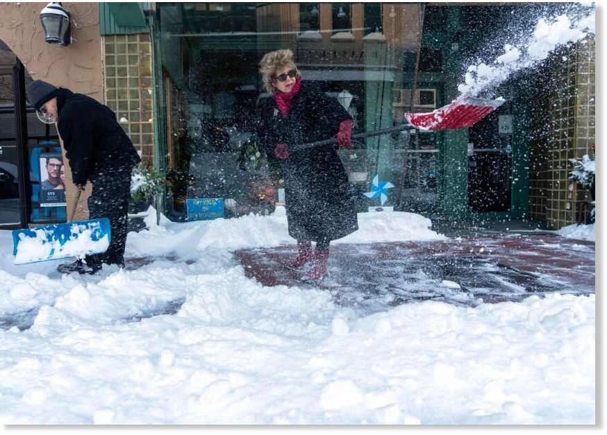 Mark and Hilary Krejcha, owners of Millers Flowers, clear the snow from in front of the store on Sixth Street in Racine, Wisconsin, on Monday.